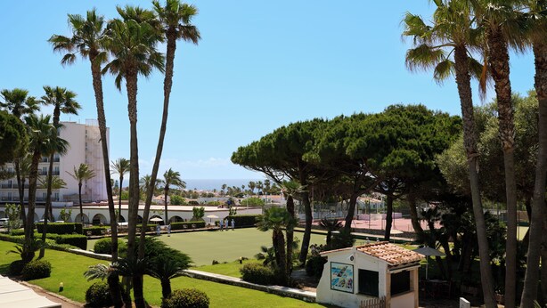 A courtyard with palm trees, a small kiosk, and a tennis court. - Aluasun Far Menorca (Sant Lluis)