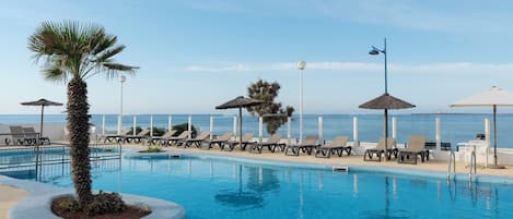 Una piscina al aire libre, sombrillas, sillones reclinables de piscina