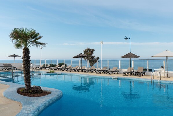 Una piscina al aire libre, sombrillas, sillones reclinables de piscina