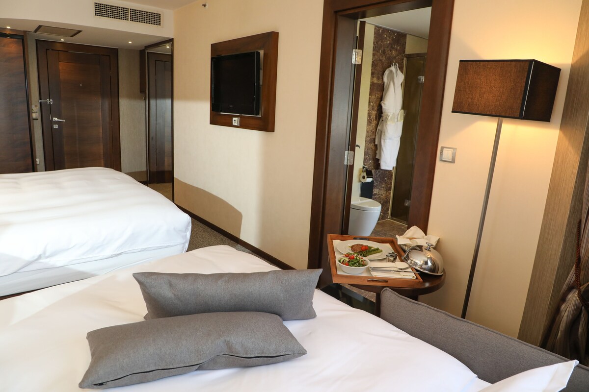 A hotel room with two beds, a TV, a mirror, a tray table with breakfast, and a wardrobe.