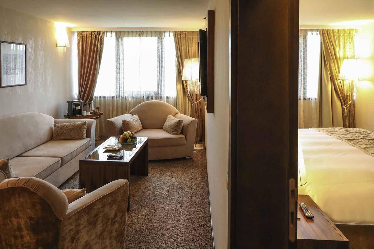 A hotel room with a sofa, a coffee table, a TV, and a bed.