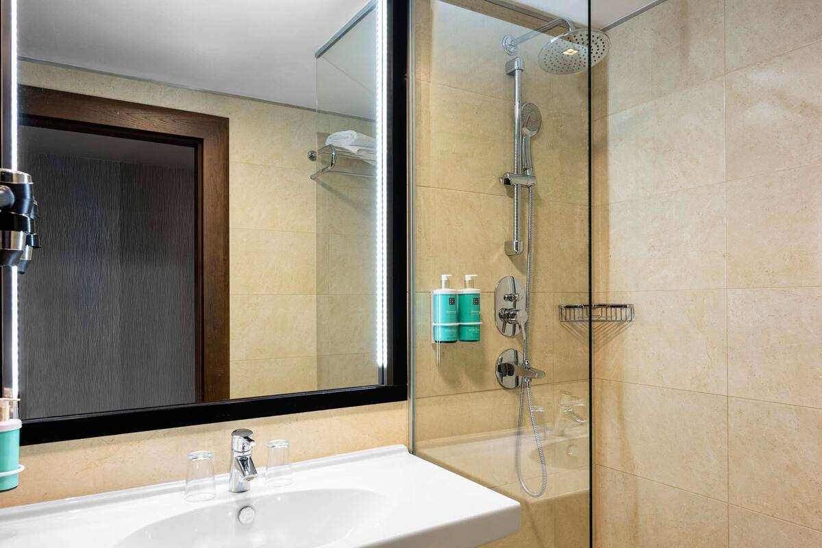 A bathroom with a glass shower enclosure, a white sink, and a mirror.