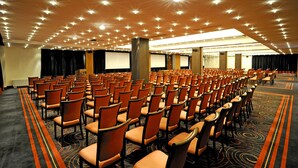A large conference room with rows of orange chairs, a carpeted floor, and a ceiling with numerous lights. -  Movenpick hotel Sarajevo (Sarajevo)