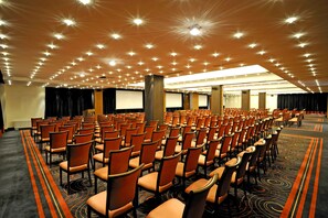 A large conference room with rows of orange chairs, a carpeted floor, and a ceiling with numerous lights. - Movenpick hotel Sarajevo (Sarajevo)
