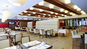 A modern restaurant with wooden beams, white tables, and chairs. - Movenpick hotel Sarajevo (Sarajevo)