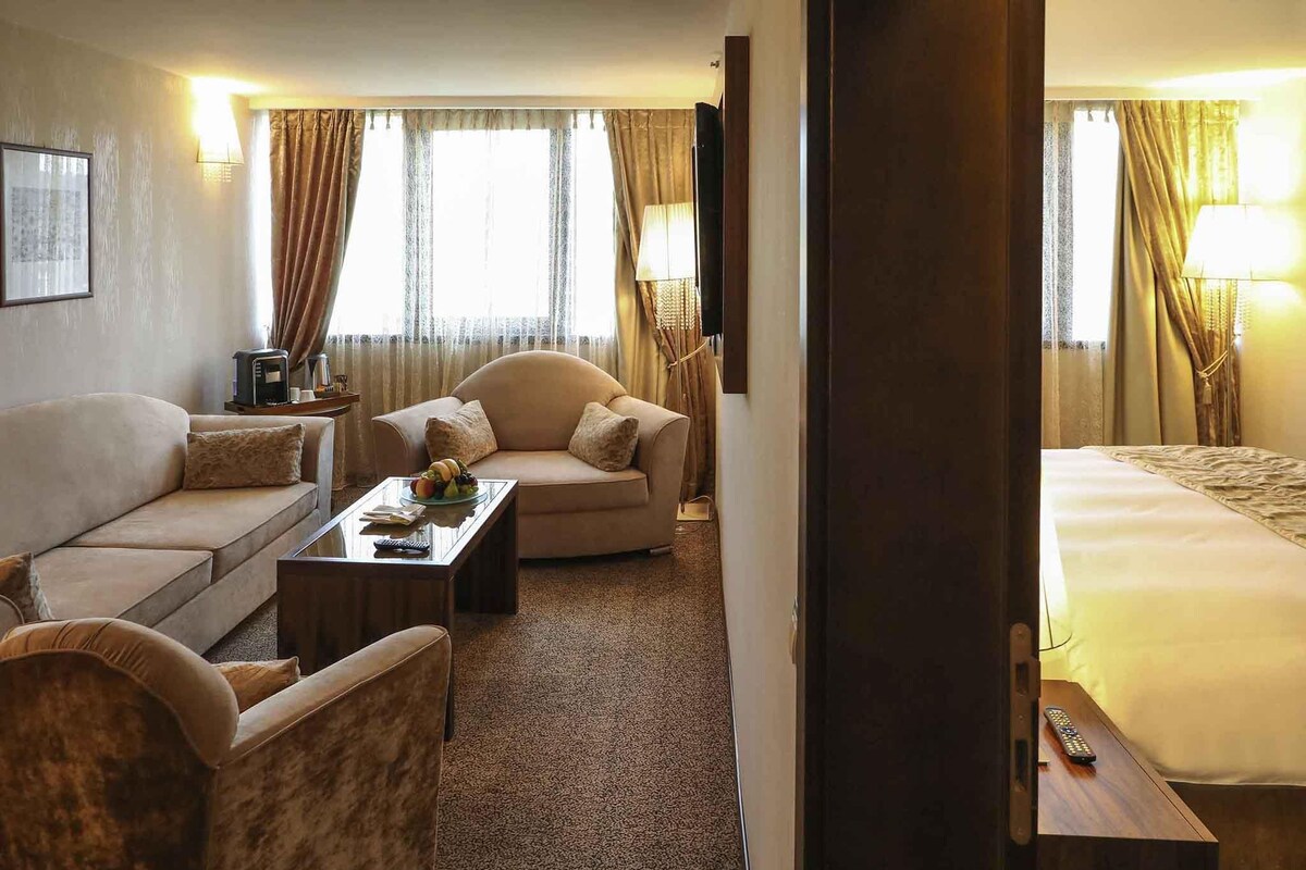 A hotel room with a sofa, a coffee table, a TV, and a bed.