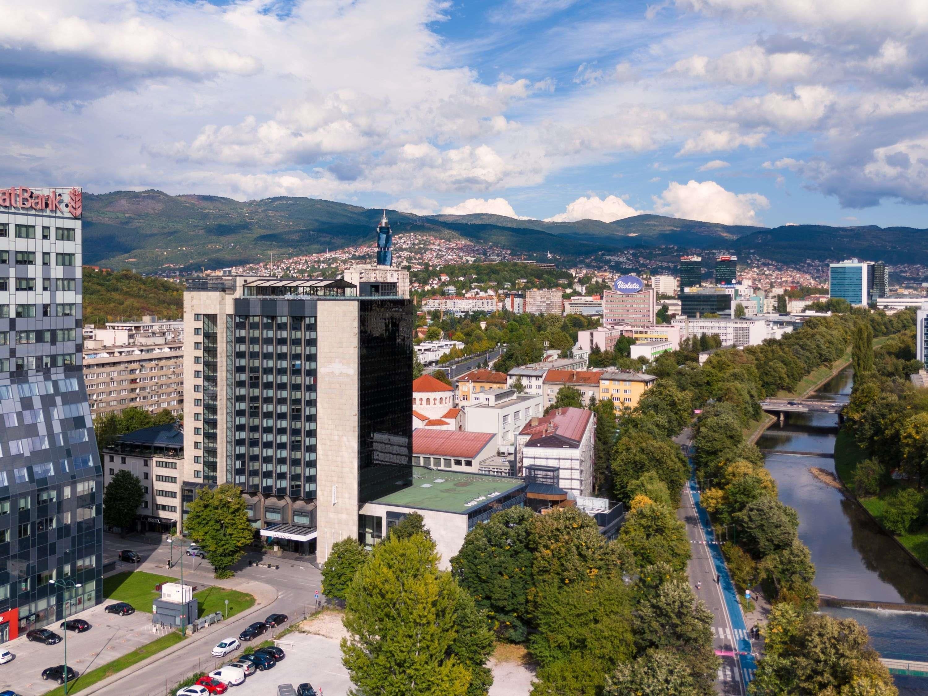 A cityscape with modern buildings, a river, and a mountainous backdrop.