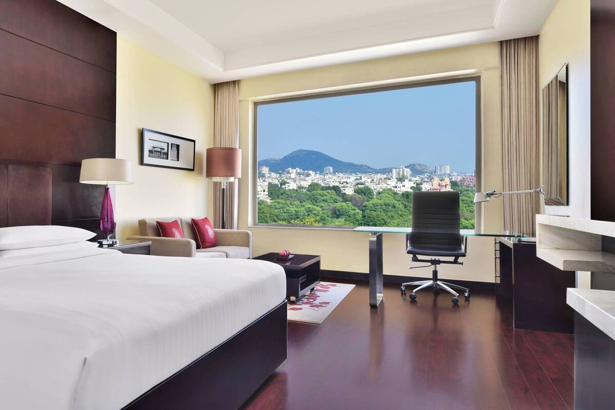 A hotel room with a large bed, a desk, a chair, and a view of a cityscape.