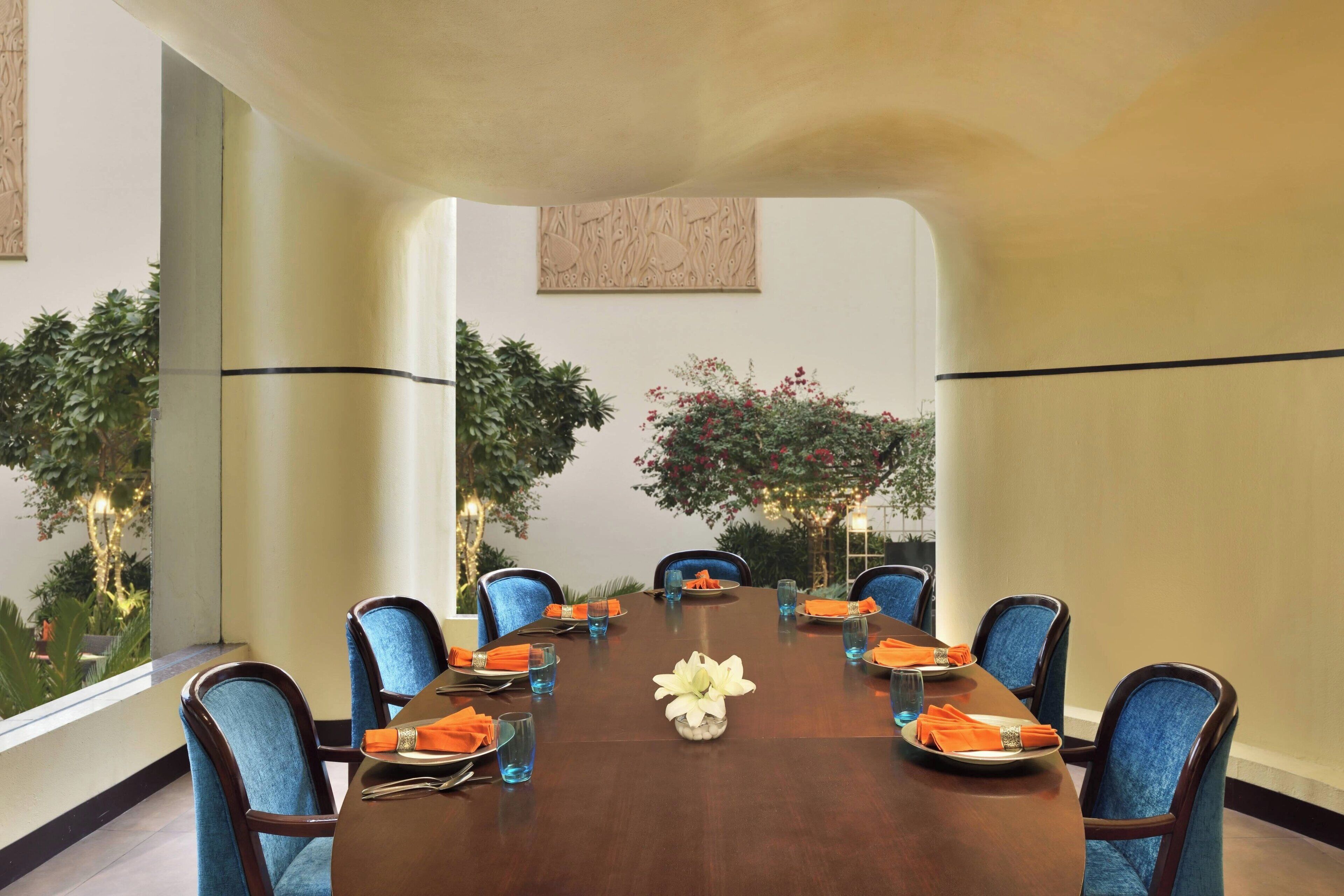 A conference room with a long table, blue upholstered chairs, and orange napkins.