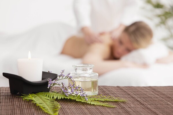 A spa setting with a candle, a bottle of essential oil, and a massage table in the background.