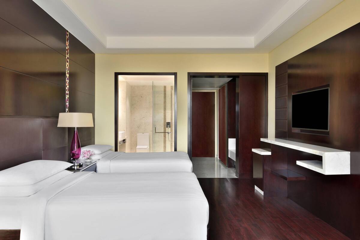 A modern hotel room with a large bed, a TV mounted on the wall, and a bathroom visible through an open door.