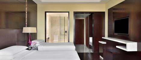 Habitación de hotel moderna con una cama grande, un televisor montado en la pared y un baño visible a través de una puerta abierta.
