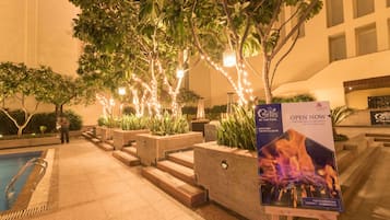 Uma área de piscina ao ar livre com escadas que levam a um edifício, cercada por árvores e iluminada por luzes de Natal.