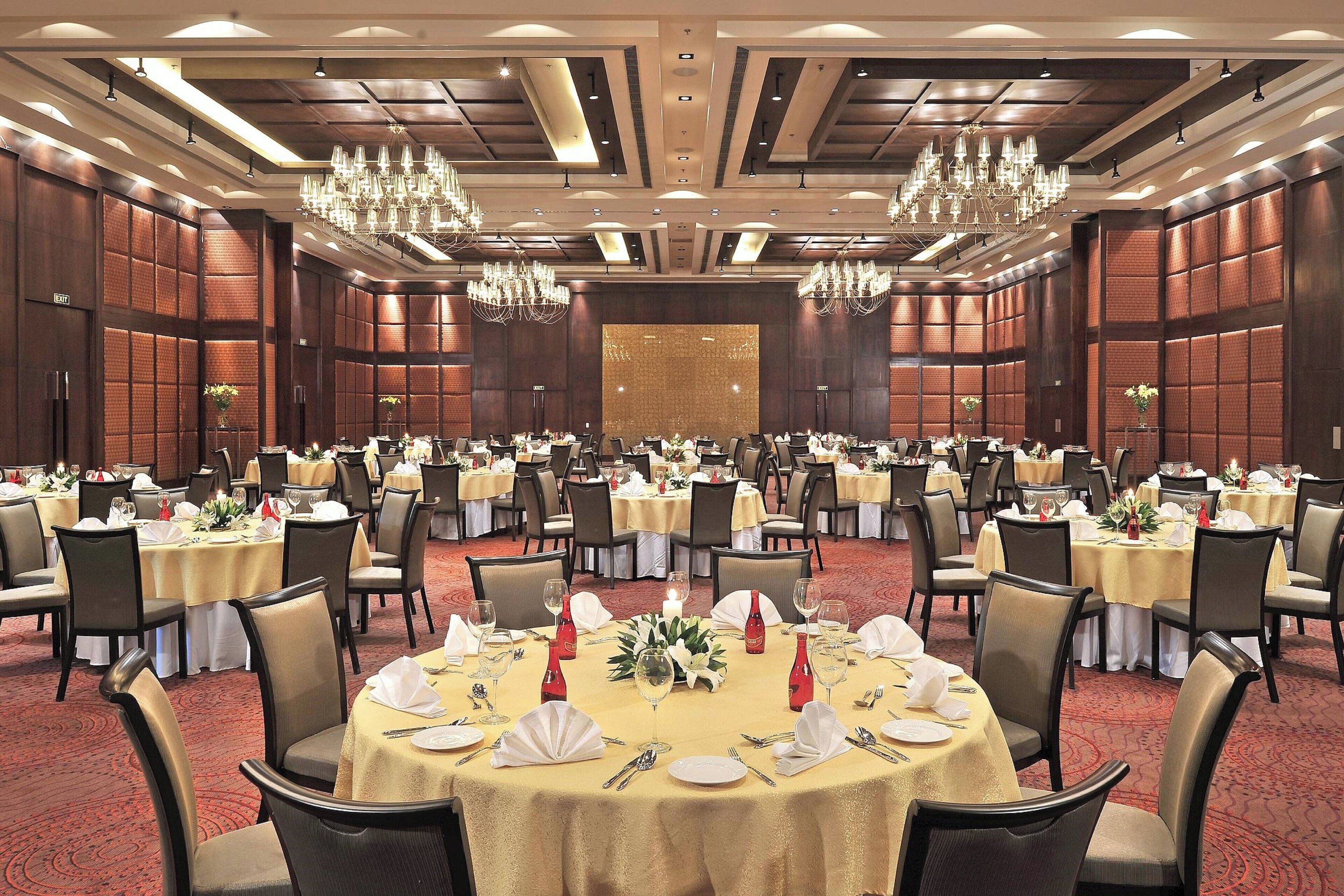 Un salón de banquetes con mesas redondas dispuestas para comer, candelabros y una gran decoración en la pared.
