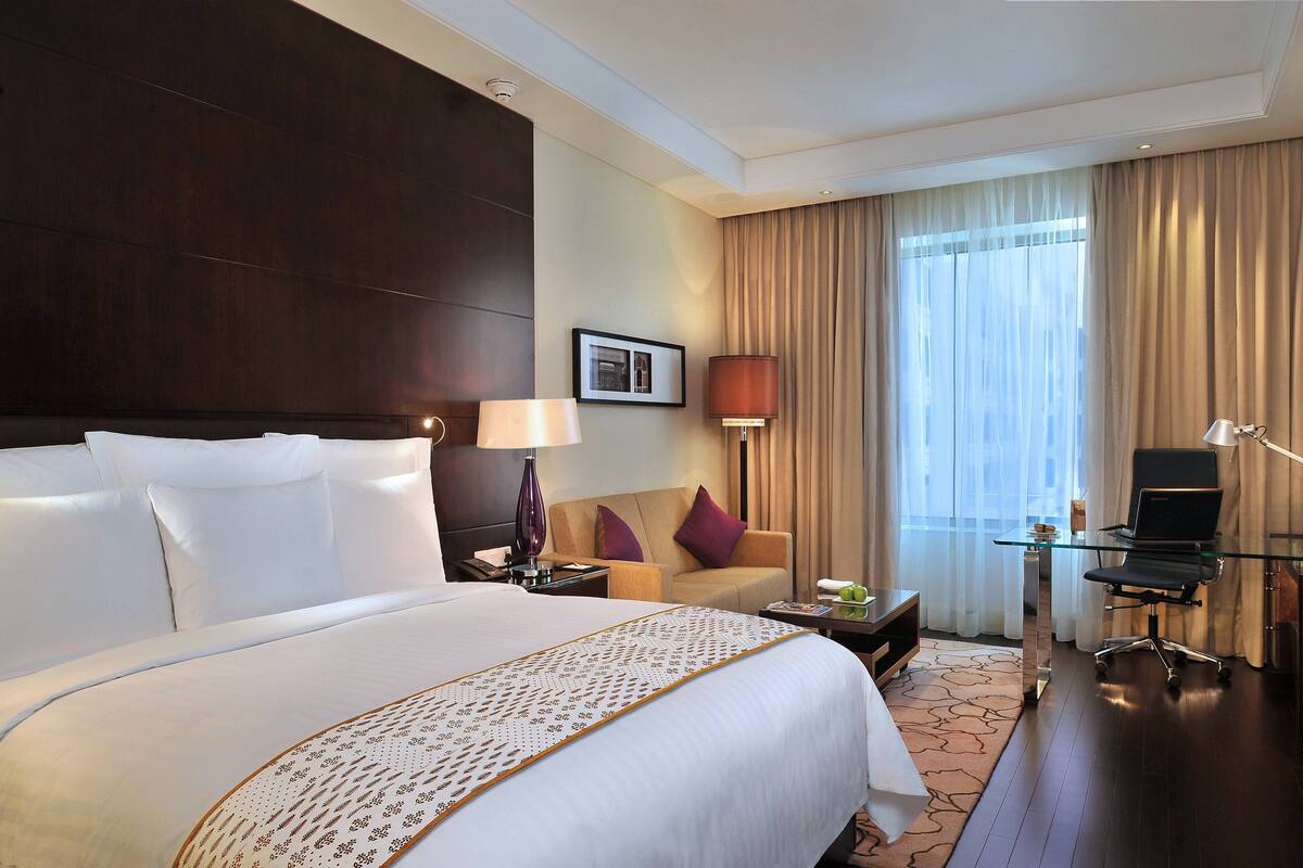 A hotel room with a large bed, a desk with a chair, a sofa, and a window with curtains.