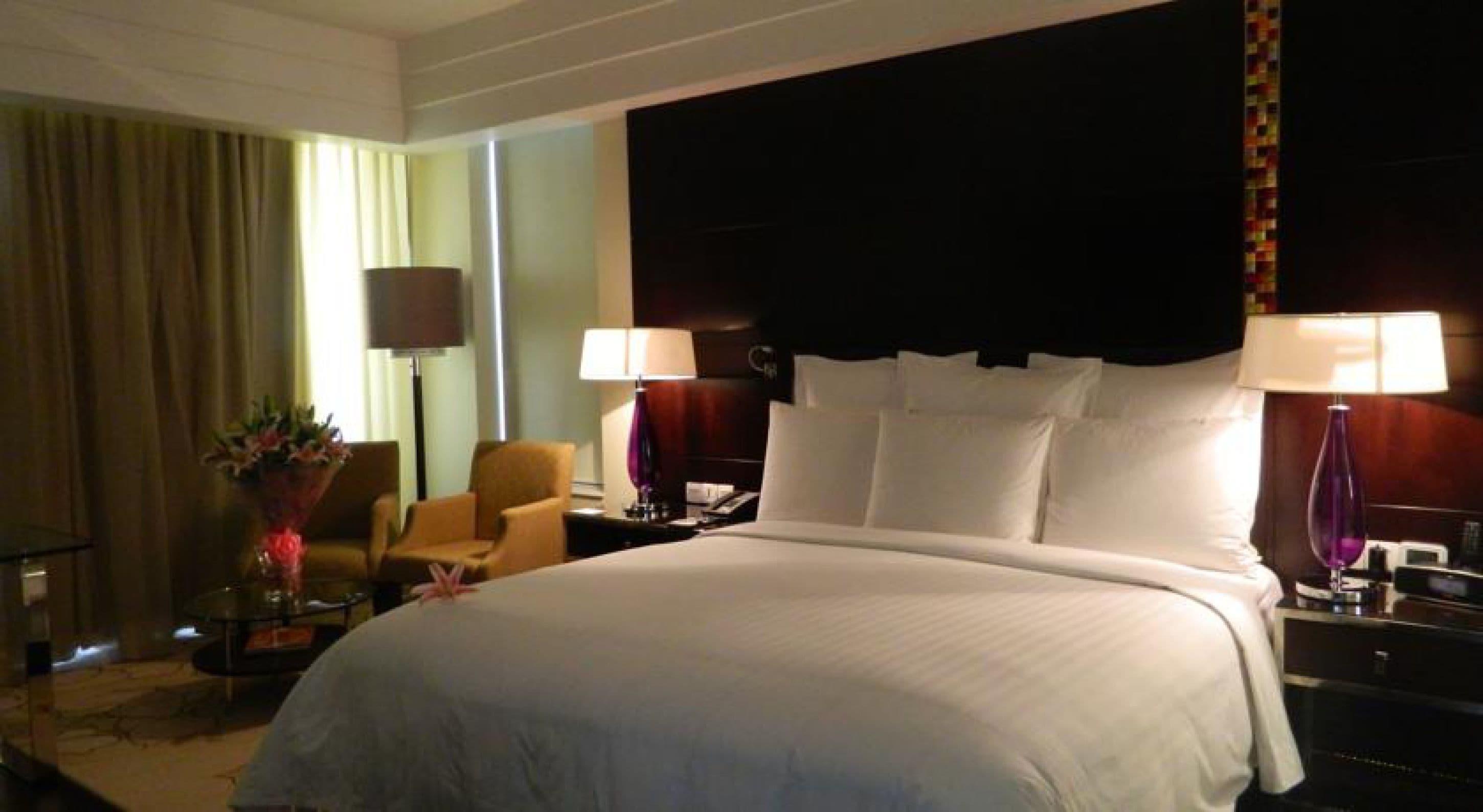 A hotel room with a large bed, two bedside tables, a chair, a lamp, and a curtain.