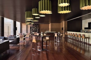 Zona de bar moderna con suelo de madera, taburetes y lámparas colgantes.