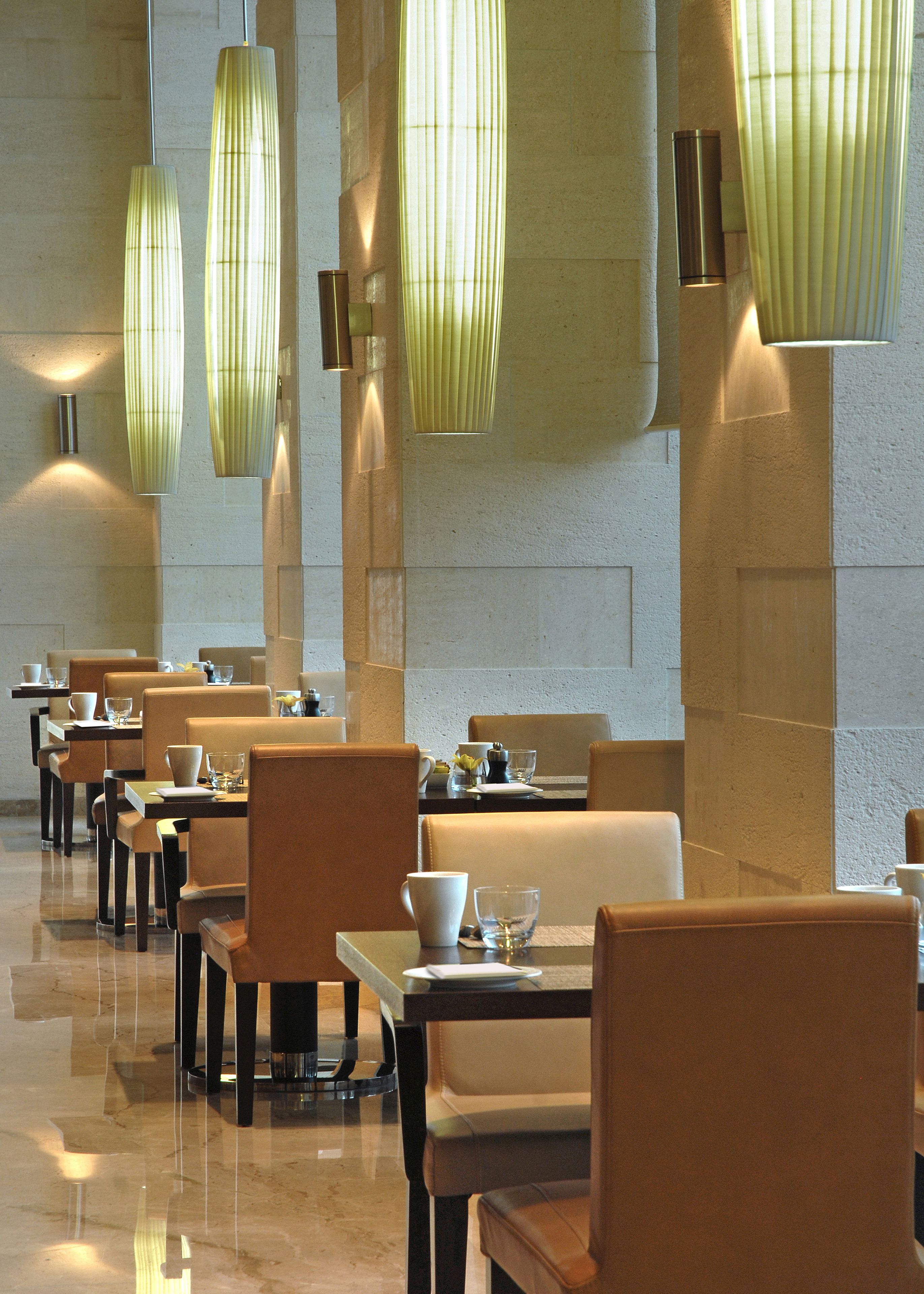 A spacious dining area with multiple tables and chairs, illuminated by modern pendant lights.