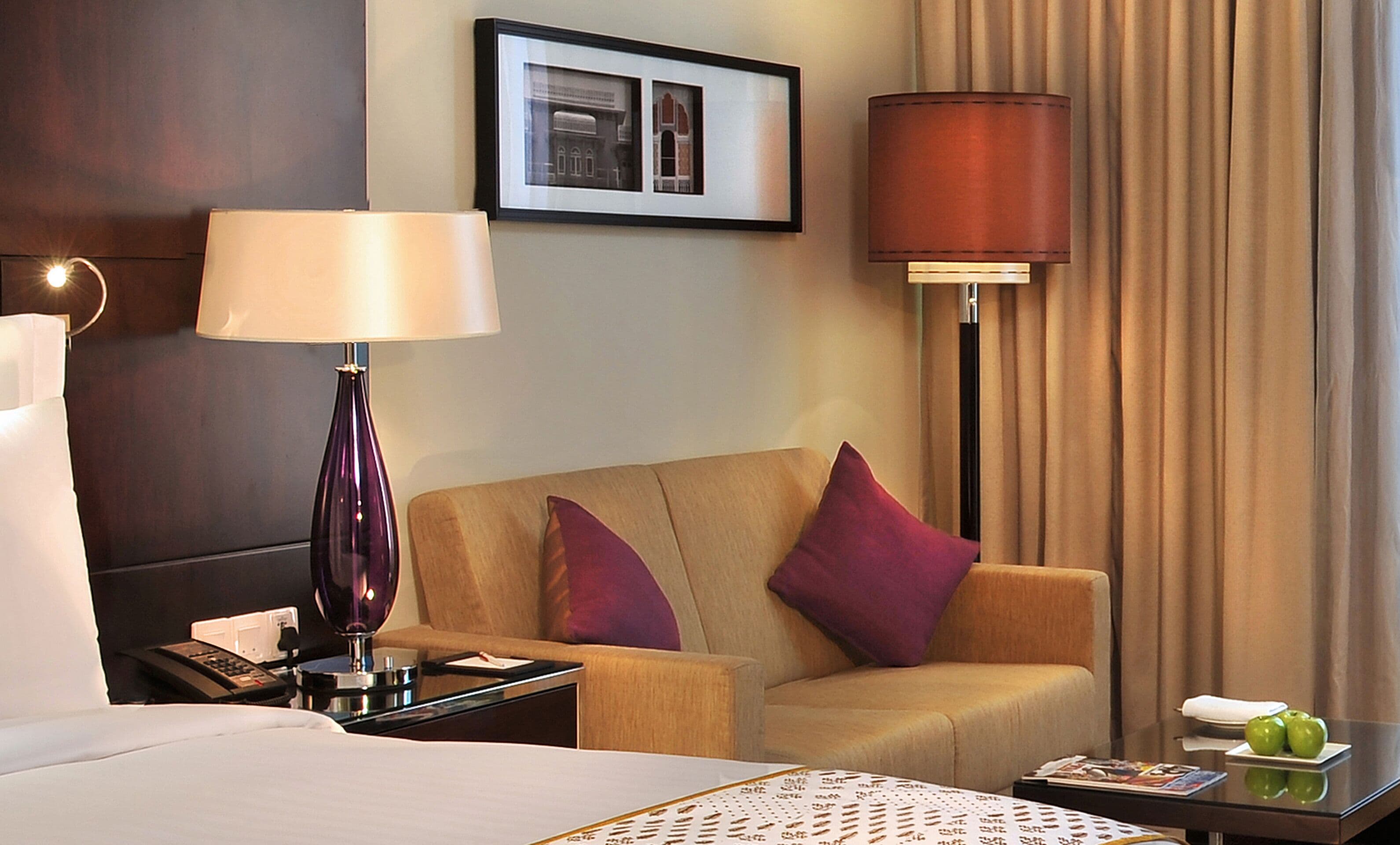A hotel room with a bed, a desk, a chair, a lamp, and a framed picture on the wall.
