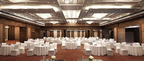 A large banquet hall with round tables and white chairs, chandeliers, and a red carpet.
