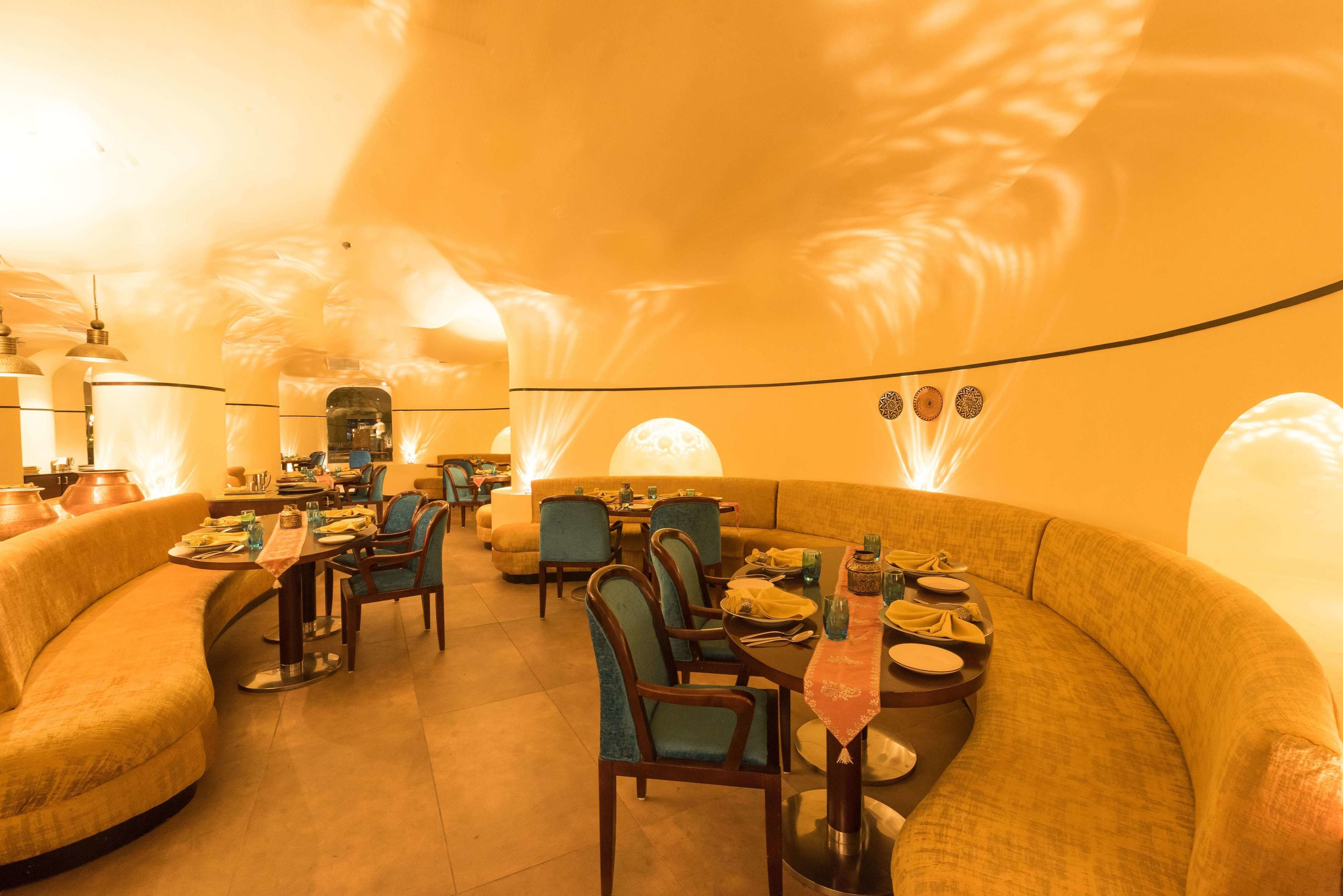 Un restaurant avec des tables et des chaises rondes, un canapé incurvé et un éclairage doux et chaleureux.