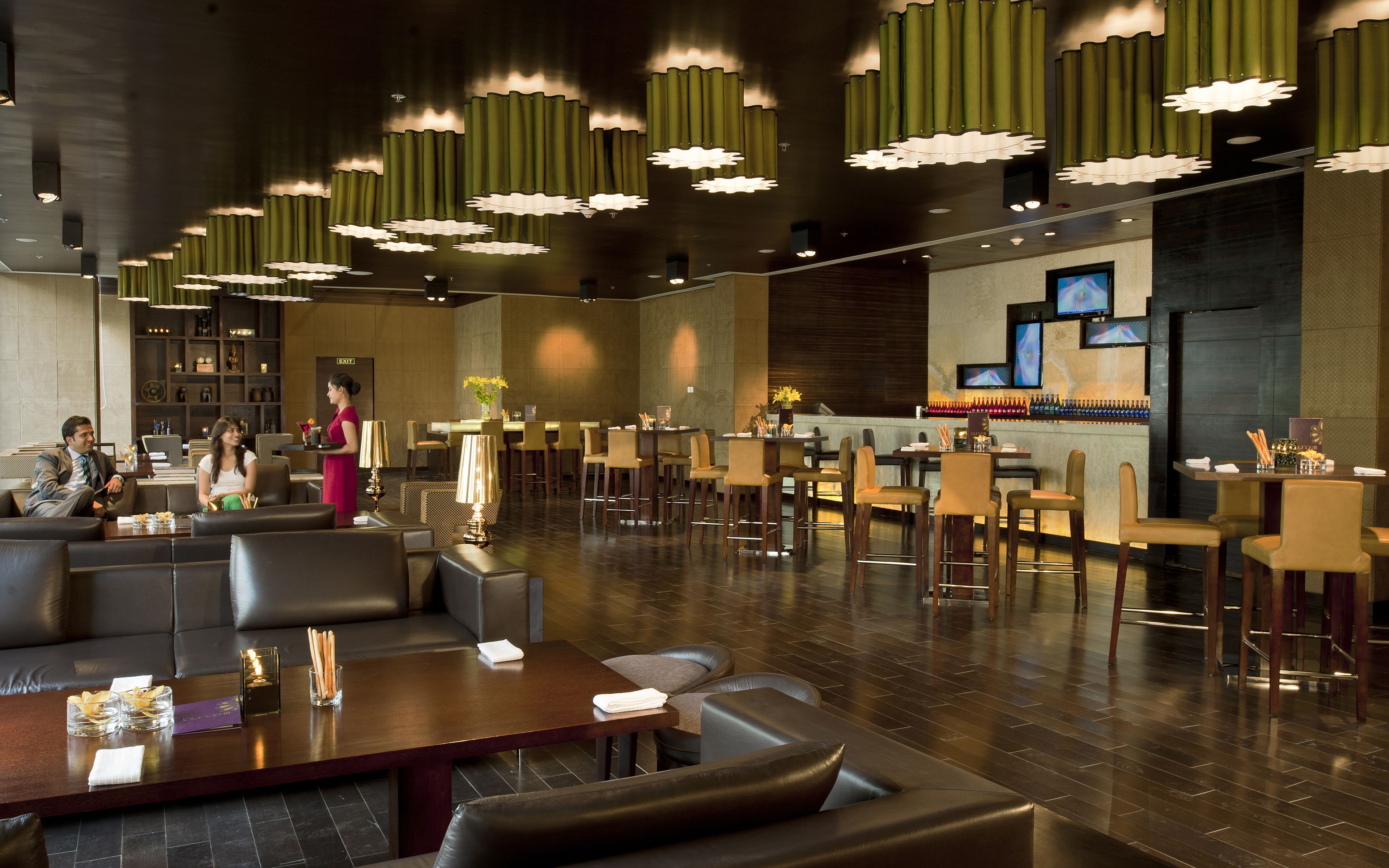 A modern hotel lobby with leather seating, a bar area, and a reception desk.