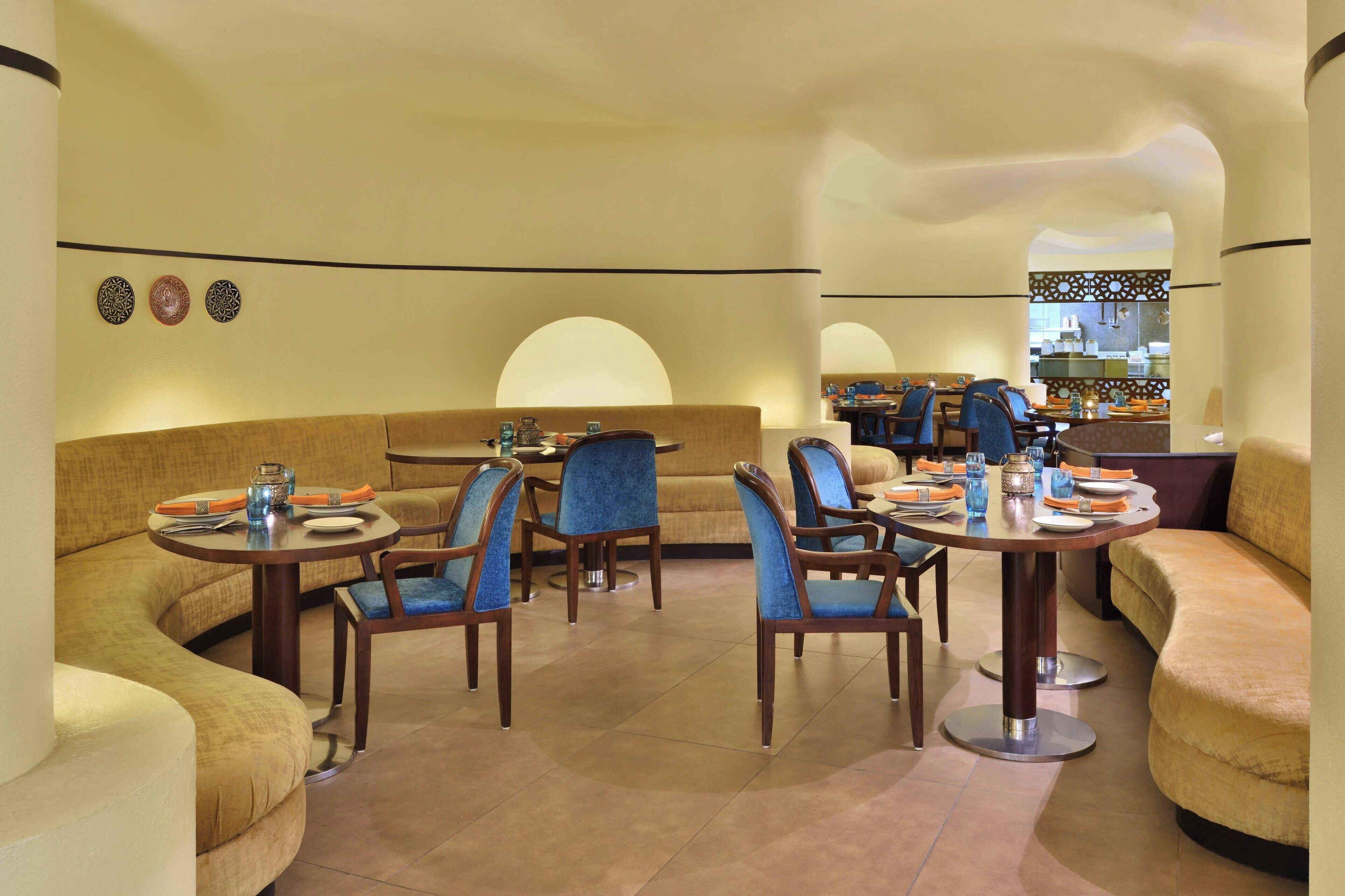 A modern dining area with round tables, blue upholstered chairs, and a curved sofa.