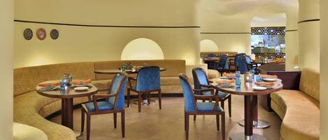 A modern dining area with round tables, blue upholstered chairs, and a curved sofa.
