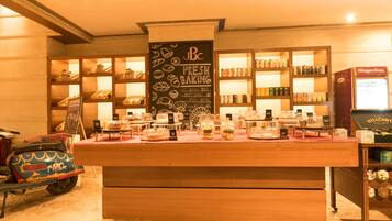 Balcão de pastelaria com produtos de panificação frescos, prateleiras com produtos embalados e uma scooter vintage.
