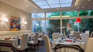 Ein Restaurant mit gedeckten Tischen, einer Wanddekoration im 'SURF'-Design und großen Fenstern mit Blick auf Grünflächen.