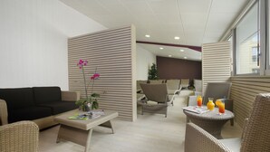 Ein stilvoller Lounge-Bereich mit Korbmöbeln, einer Topfpflanze mit Orchideen und einem Tisch mit Getränken und Zeitschriften.