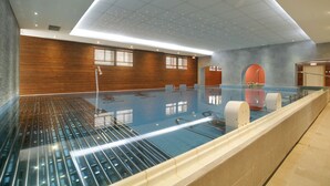 Ein moderner, überdachter Schwimmbereich mit Glasboden, Holzpaneelen und einer Decke mit Einbaustrahlern.