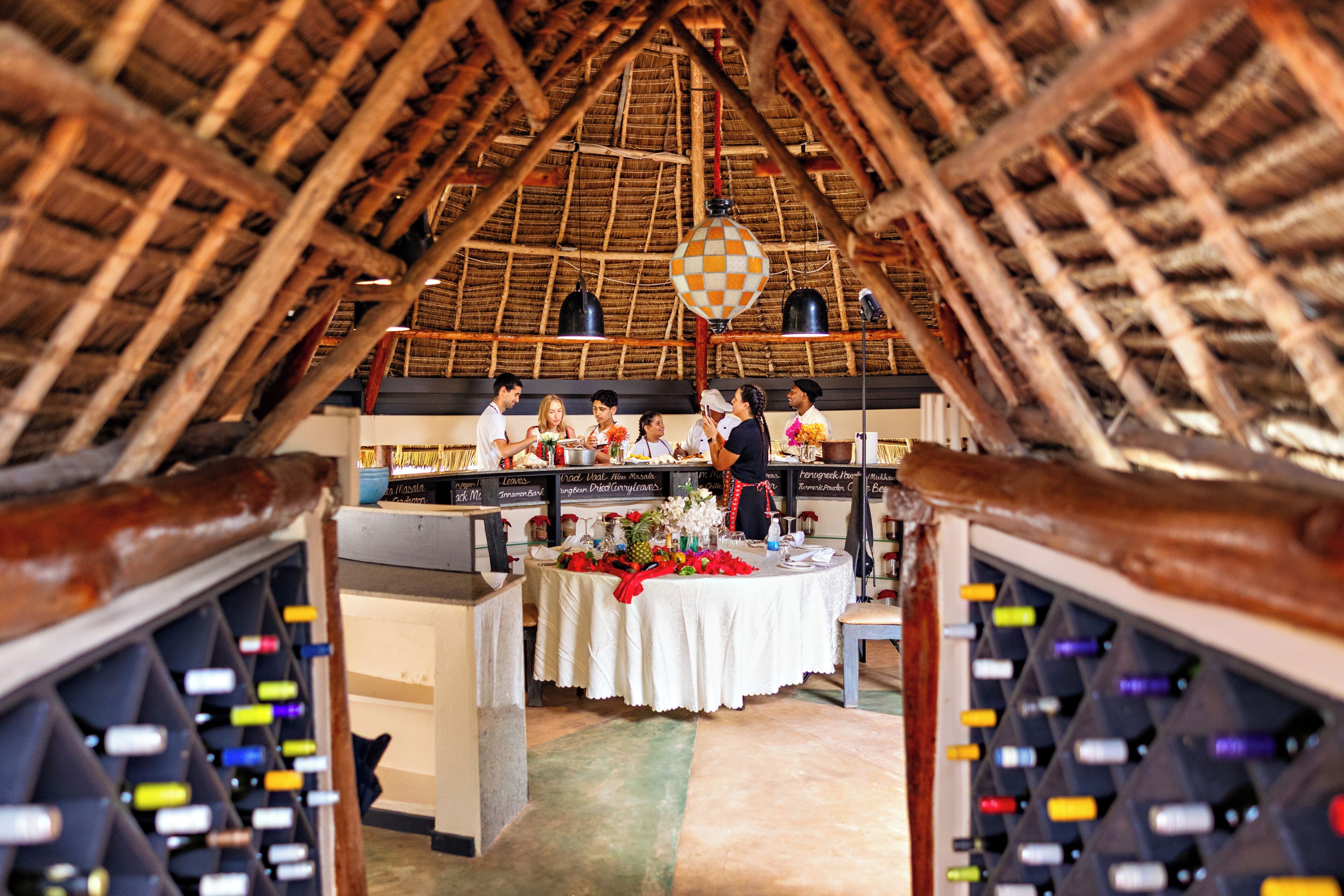 Un intérieur caractérisé par un plafond haut, des poutres en bois, une table recouverte d’une nappe blanche et des bouteilles de vin.