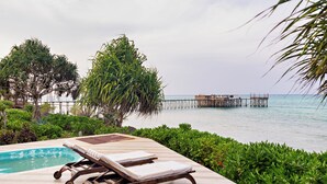 A poolside area with lounge chairs, a wooden deck, and a view of the sea and a pier. - Essque Zalu Zanzibar (Nungwi)