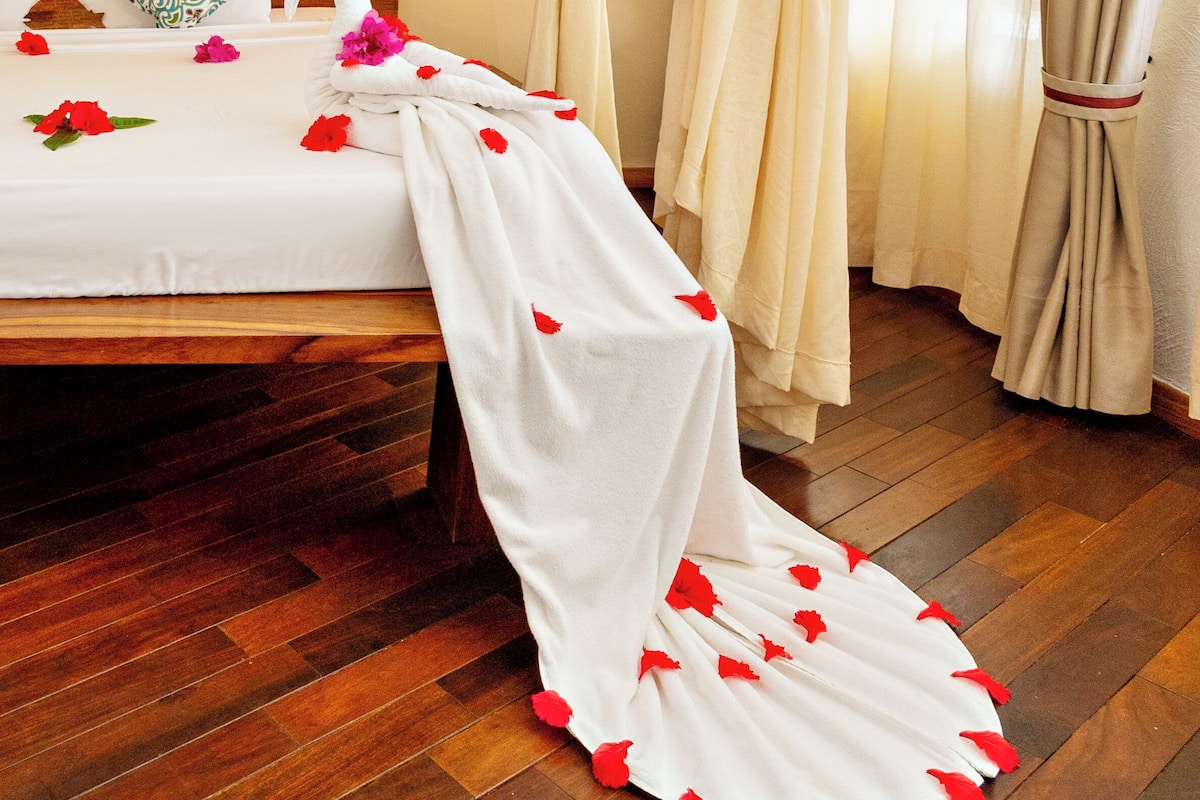 A hotel room with a bed, curtains, a wall-mounted light, and wooden flooring.