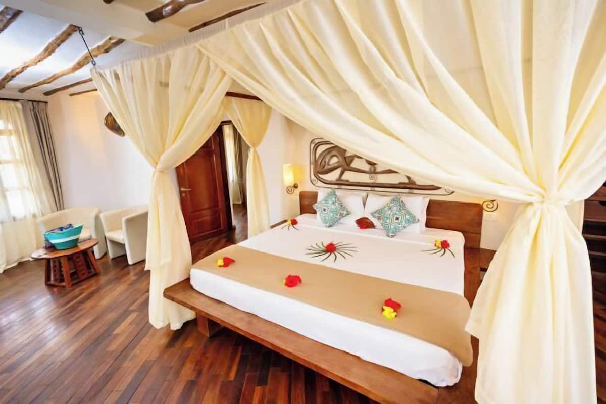 A bed with a canopy, a bedside table, and a chair in a room with wooden flooring.