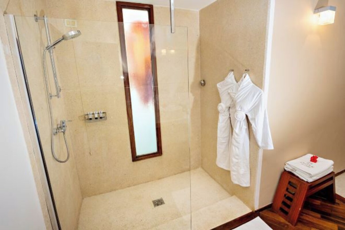 A modern bathroom with a glass-enclosed shower, a wooden stool with towels, and a mirror.