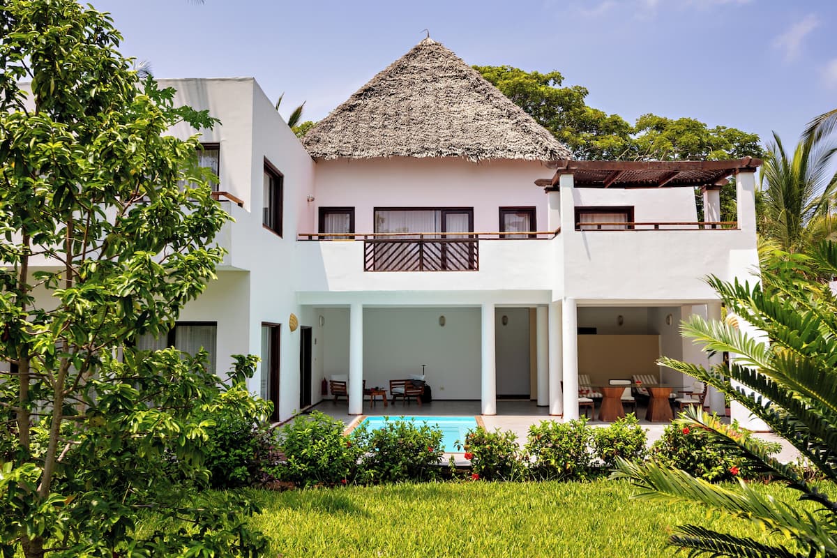 A two-story house with a thatched roof, a swimming pool, and a covered patio area.