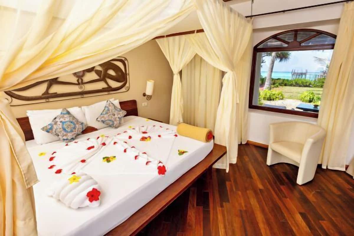 A bed with a canopy, a chair, and a view of the ocean.