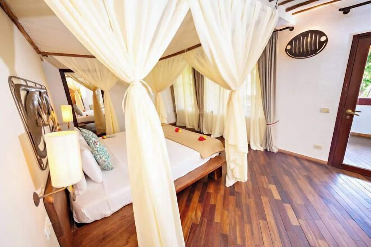 A bedroom with a bed, canopy, wooden flooring, and a door.