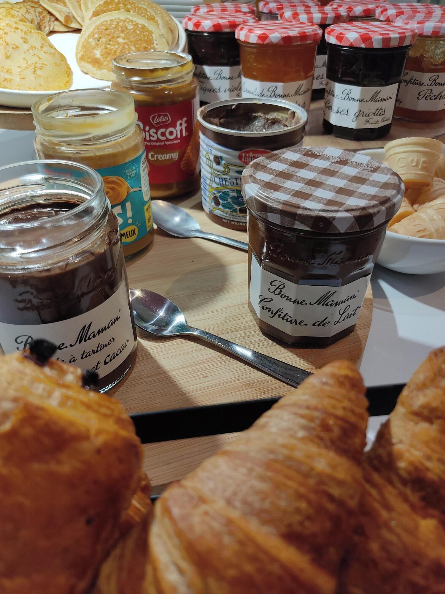 Una mesa con diversos alimentos, incluyendo pasteles, frascos de mermeladas y una cuchara.