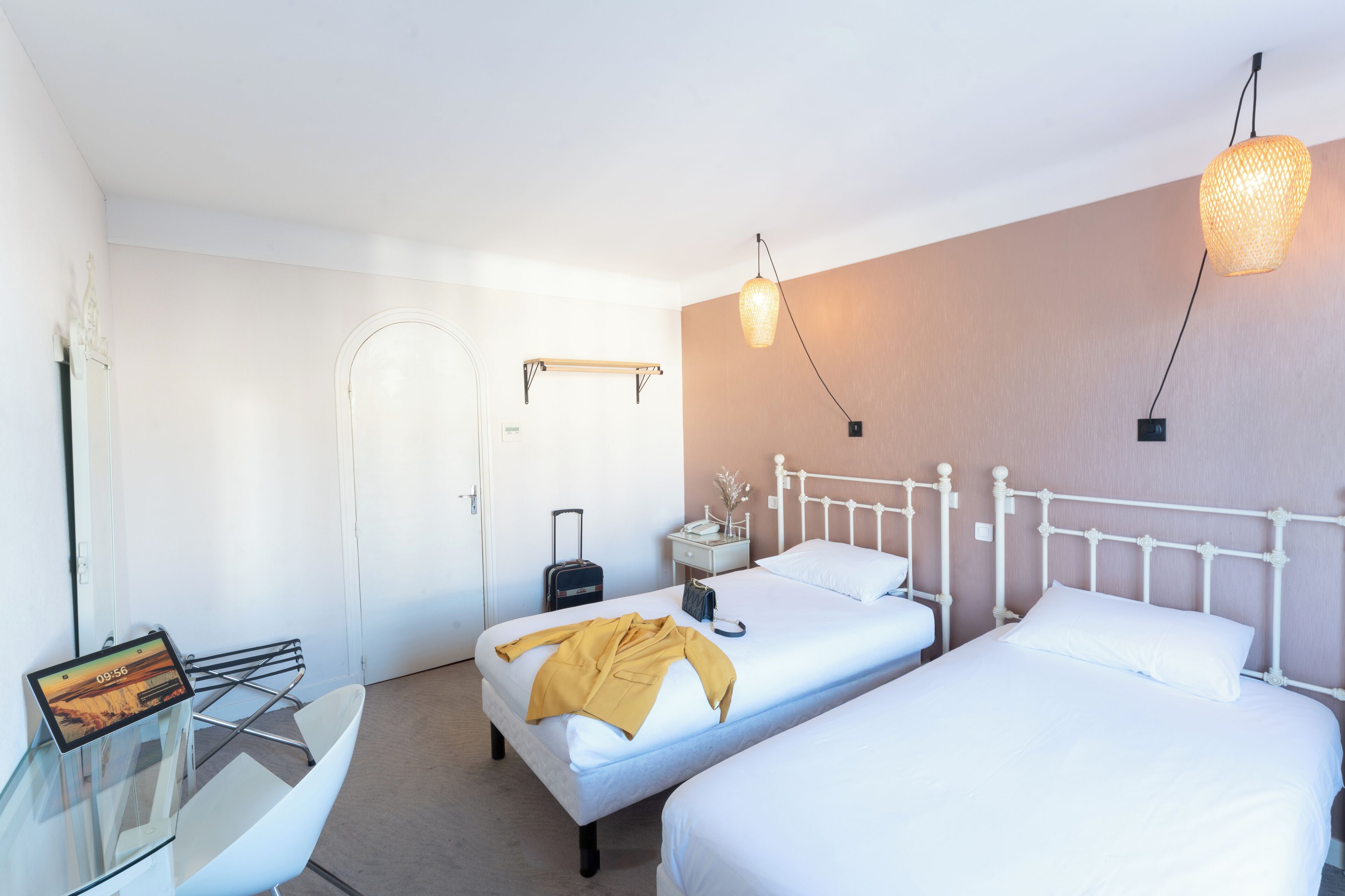Et hotelværelse med to senge, et sengebord, en lampe, en kuffert og et digitalt ur.