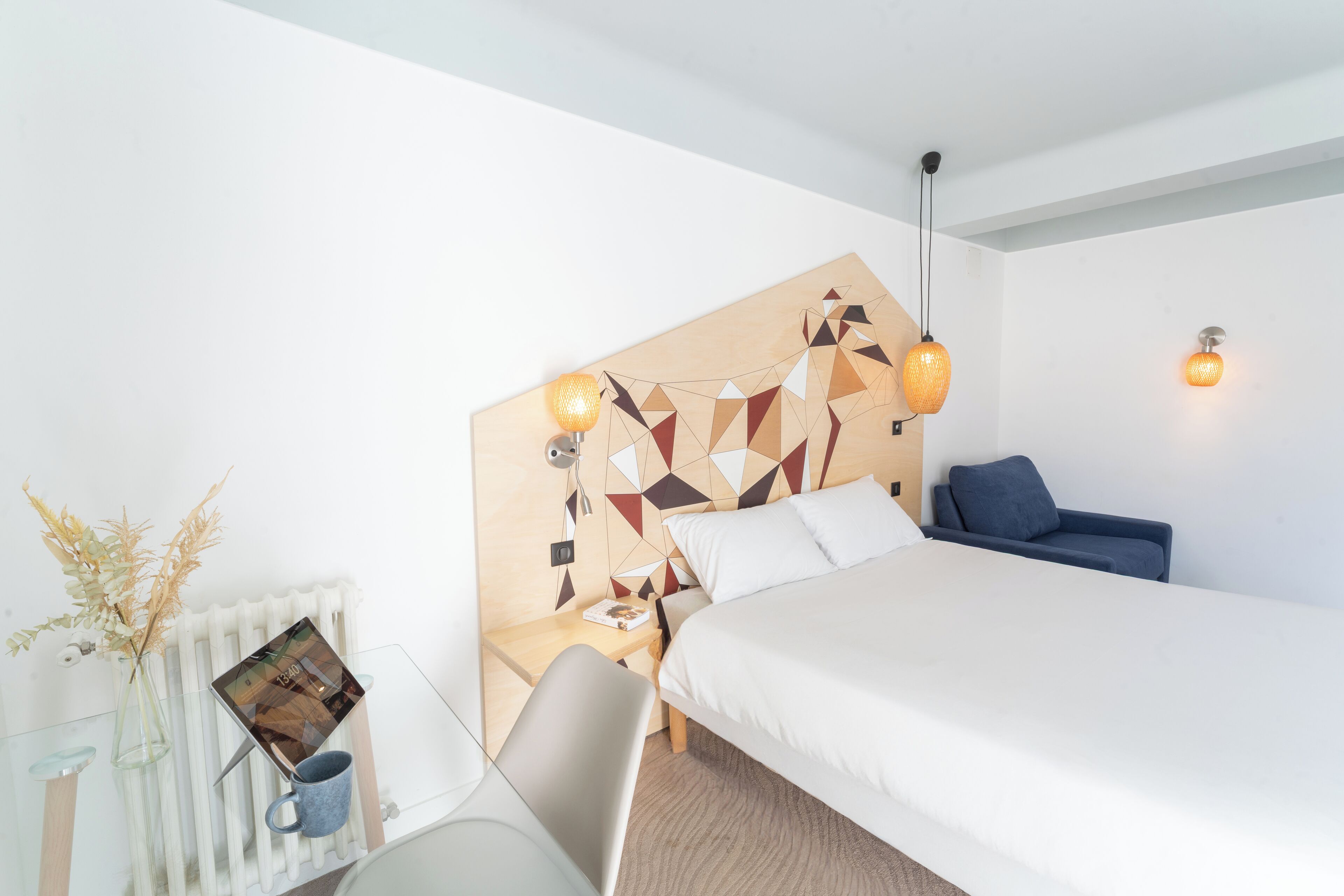 A modern hotel room with a bed, bedside table, chair, and a decorative wall panel.