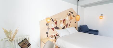 A modern hotel room with a bed, bedside table, chair, and a decorative wall panel.