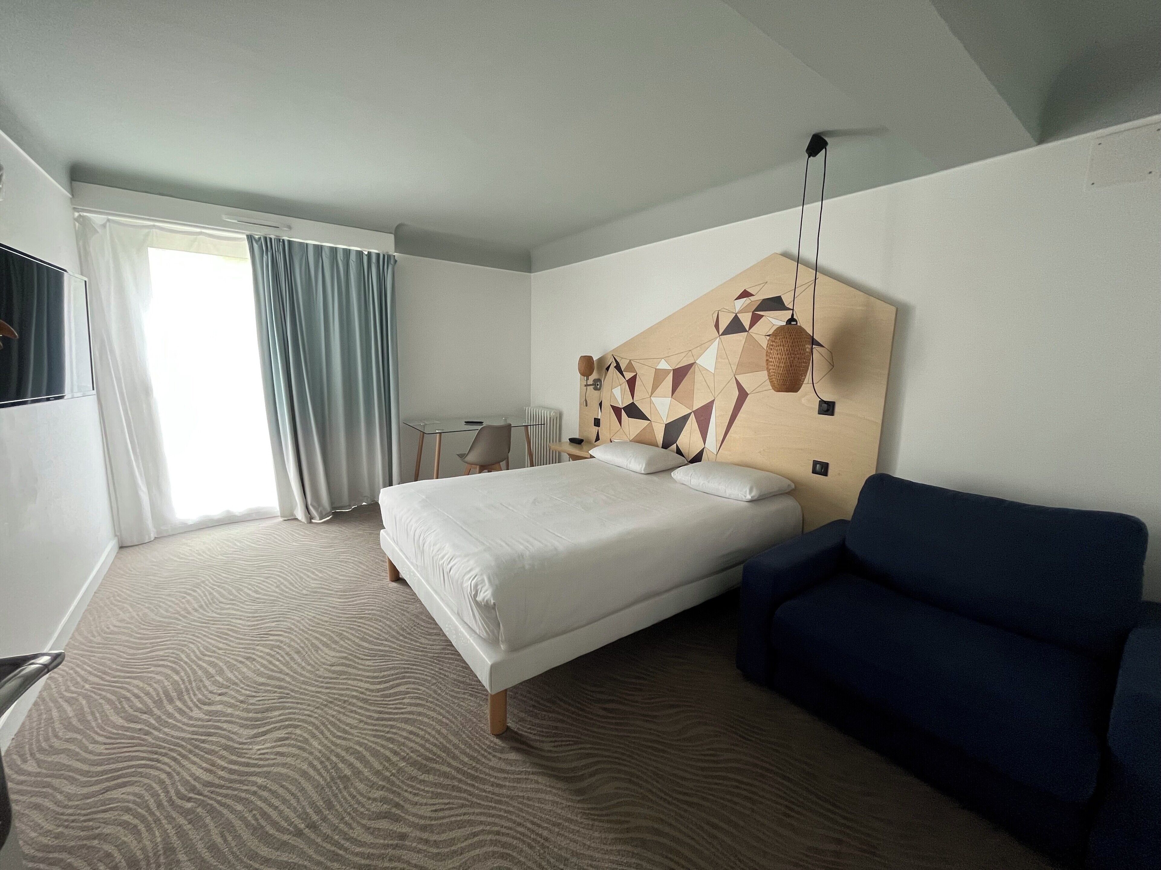 A hotel room with a bed, a blue sofa, a desk, and a TV.