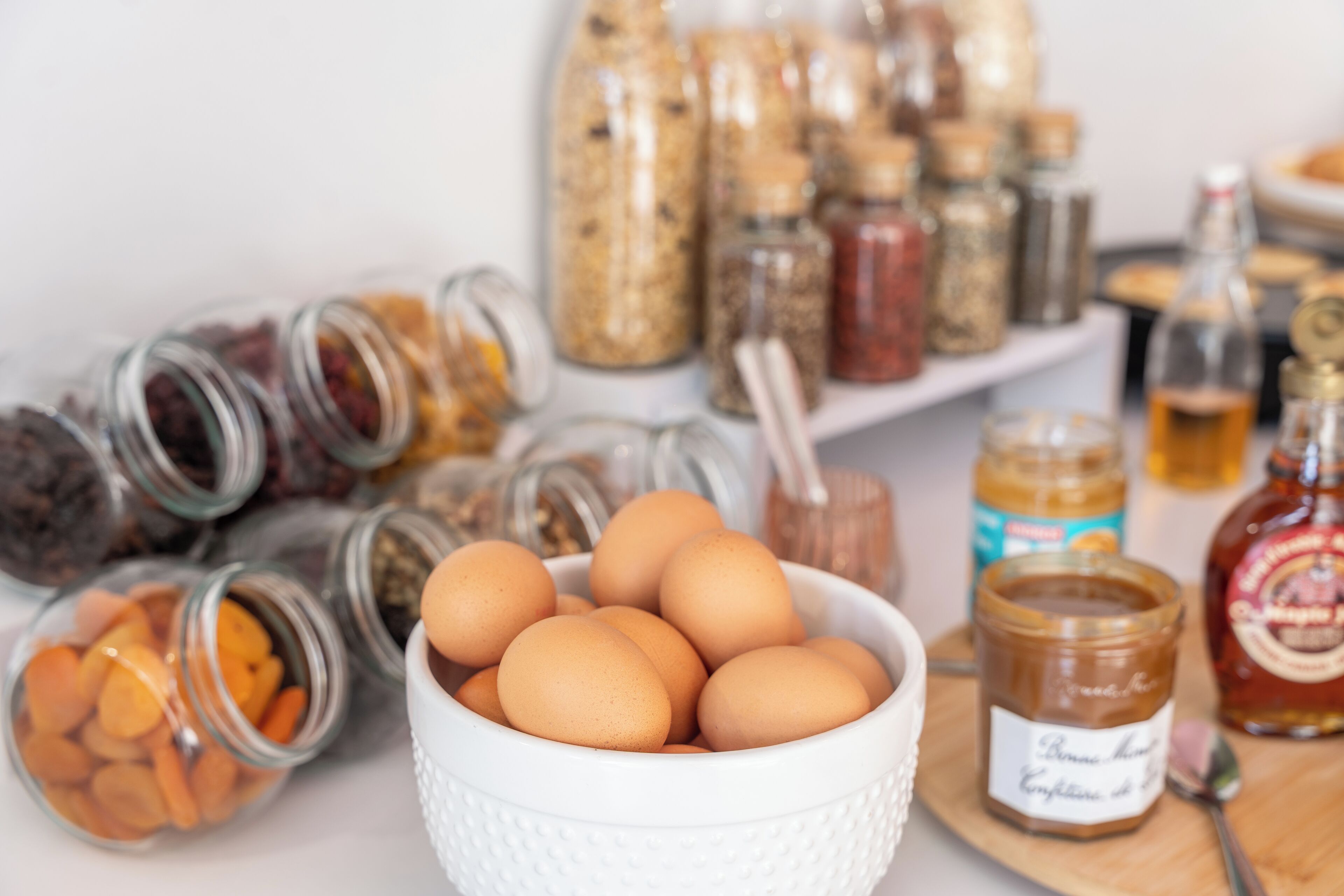 A kitchen counter with various jars of spices, a bowl of eggs, and a bottle of honey.