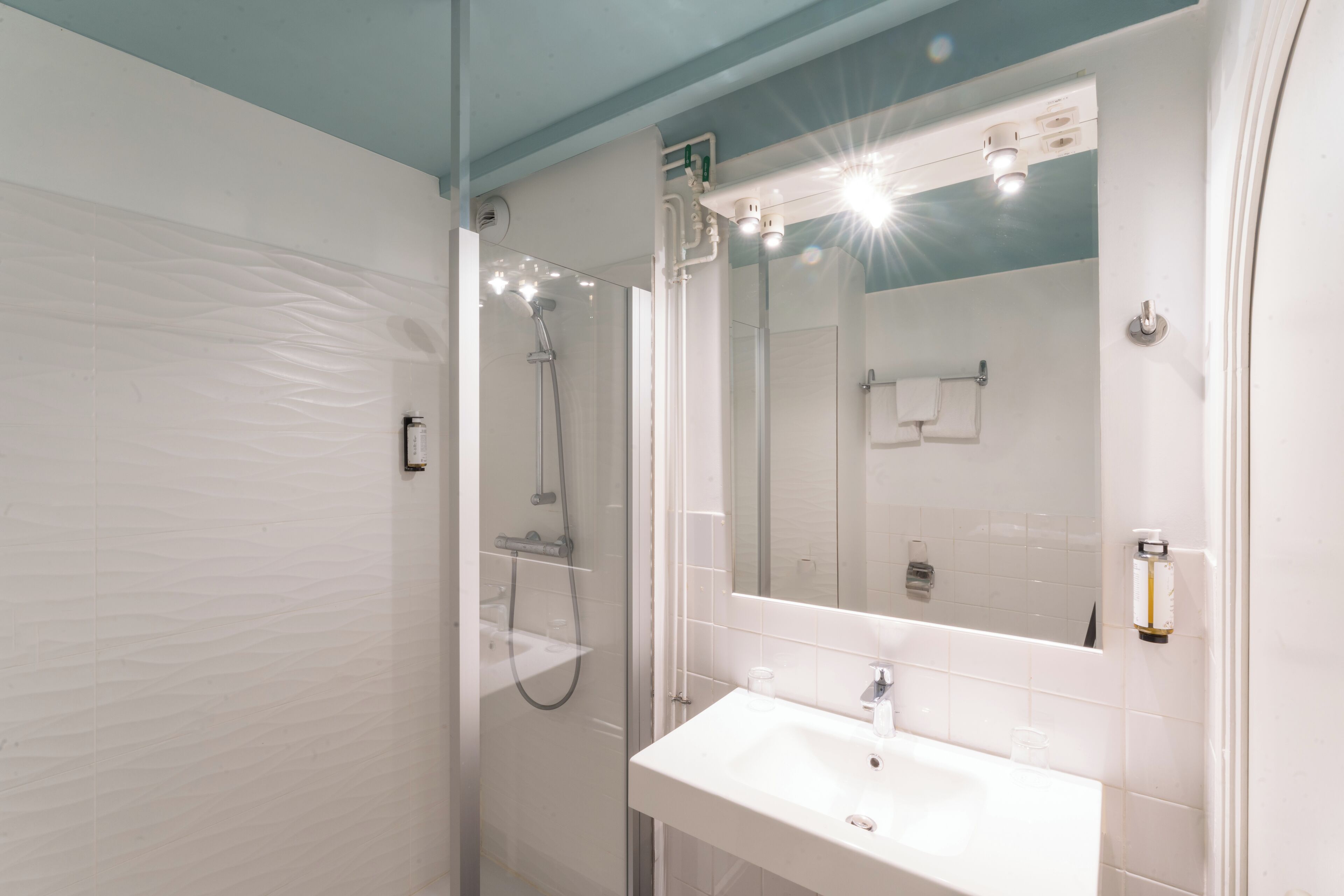 A modern bathroom with a glass-enclosed shower, a white sink, and a large mirror.