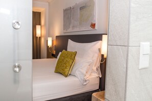 Una habitación de hotel con una cama bien hecha, cabecera, dos lámparas fijadas a la pared y un cuadro sobre la cama.