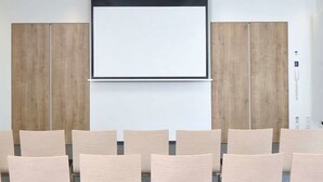 Un salón de conferencias con una pantalla de proyección grande, paneles de madera y filas de sillas.