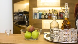 Una zona de bar con una barra de madera, un bol de vidrio con manzanas verdes, una botella y varios vasos.